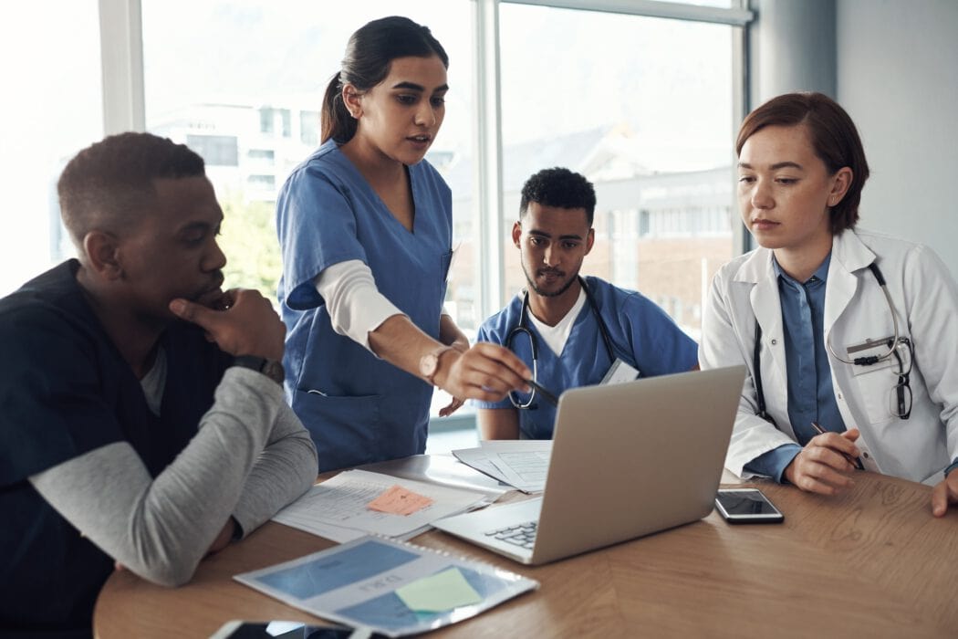 Four medical professionals, including emergency room physicians from EPPA Health, are in discussion around a table with laptops and documents, focused on a screen.