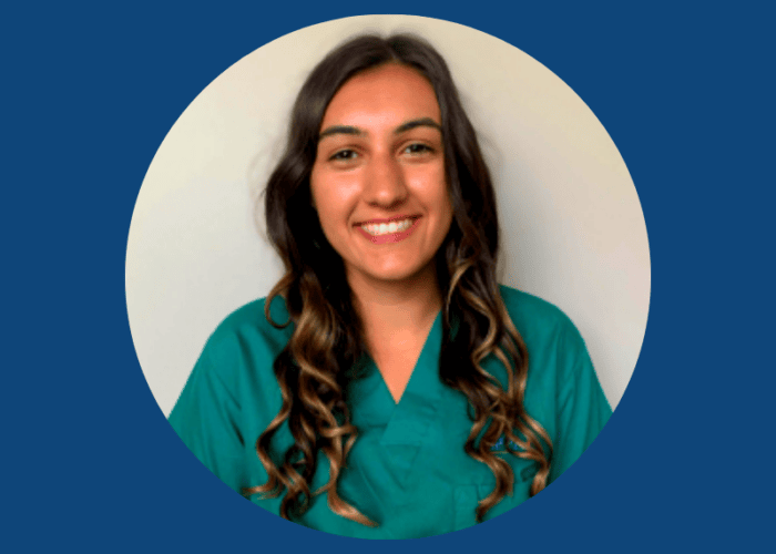 A woman with long wavy hair is smiling, wearing a green scrub top, set against a plain background within a circular blue frame, representing EPPA Health's dedicated team of emergency room physicians in Minnesota hospitals.