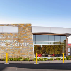 Exterior view of Allina Health Cambridge Medical Center includes the ambulance entrance on the right and stone facade with logo on the left, a proud part of Minnesota Hospitals served by expert Emergency Room Physicians.