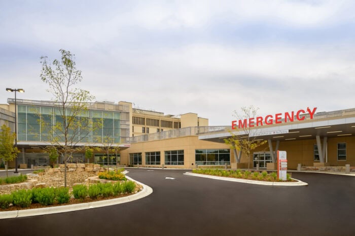 The EPPA Health emergency entrance features a large red "EMERGENCY" sign, surrounded by landscaped gardens and a paved driveway under the typically cloudy Minnesota sky.