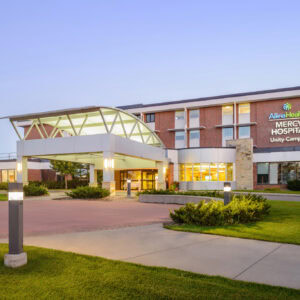Front view of a modern hospital building with a large entrance, where "Allina Health Mercy Hospital Unity Campus" proudly stands. Surrounded by grass and pathways, this Minnesota hospital also houses EPPA Health's expert Emergency Room Physicians, ensuring exceptional care.