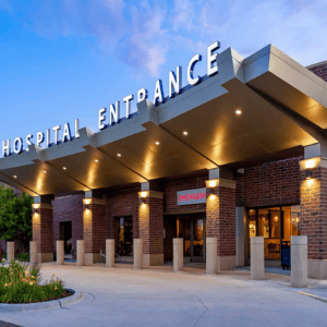 The entrance of the Minnesota Hospitals features a canopy and a prominent emergency sign guiding visitors along the pathway. Its brick exterior stands resilient, with lights illuminating the way for patients and Emergency Room Physicians from EPPA Health ready to provide crucial care.