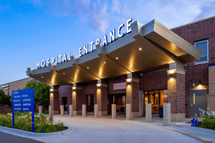 The entrance of the Minnesota Hospitals features a canopy and a prominent emergency sign guiding visitors along the pathway. Its brick exterior stands resilient, with lights illuminating the way for patients and Emergency Room Physicians from EPPA Health ready to provide crucial care.