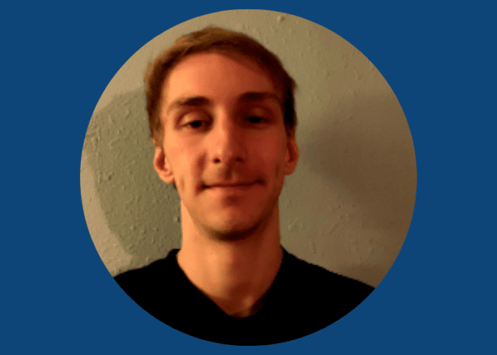 A person with short hair and a slight smile, perhaps an Emergency Room Physician, faces the camera wearing a dark shirt. The background is a plain wall with a blue circular frame.