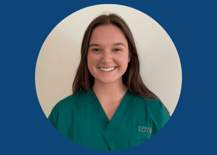 A person with long brown hair, wearing green medical scrubs with the letters 