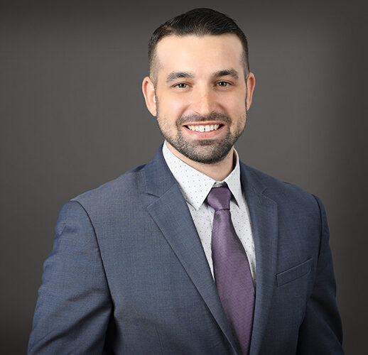 A person wearing a blue suit, white shirt, and purple tie, smiling warmly as if they just left an EPPA Health meeting, stands confidently against a gray background.