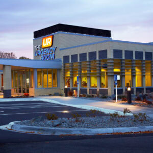 A modern urgent care building with large windows, labeled "The Urgency Room," stands quietly in an empty parking lot during dusk. Operated by EPPA Health, it exemplifies the expertise of Minnesota Hospitals and their dedicated emergency room physicians.