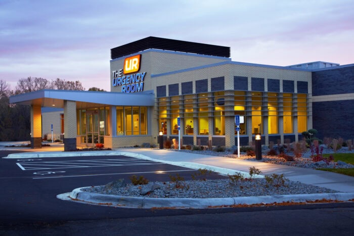 A modern urgent care building with large windows, labeled "The Urgency Room," stands quietly in an empty parking lot during dusk. Operated by EPPA Health, it exemplifies the expertise of Minnesota Hospitals and their dedicated emergency room physicians.