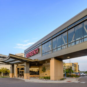 Exterior view of a Minnesota hospital entrance with a prominent "Emergency" sign and an adjoining skywalk under a clear blue sky, highlighting the dedicated Emergency Room Physicians at EPPA Health.