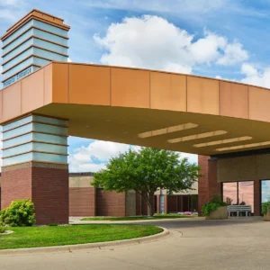 Modern building entrance with a curved orange overhang, brick columns, and surrounding greenery under a blue sky with clouds, epitomizing the innovative architecture often seen in Minnesota hospitals.