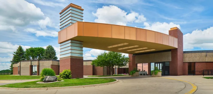 Modern building entrance with a curved orange overhang, brick columns, and surrounding greenery under a blue sky with clouds, epitomizing the innovative architecture often seen in Minnesota hospitals.