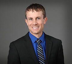 A person in a suit with a blue shirt and striped tie is smiling against a gray background, embodying the professionalism often seen at Minnesota Hospitals.