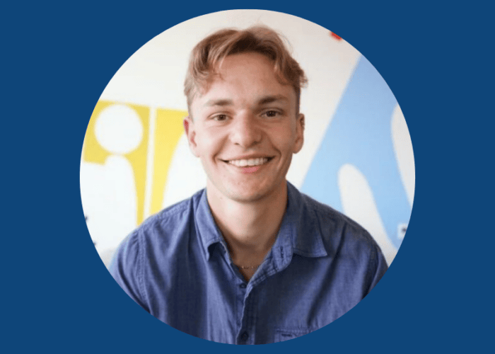 A person with light brown hair smiles in front of a blue and yellow abstract background, wearing a blue shirt. The backdrop subtly reflects the vibrant energy often seen in Minnesota Hospitals' Emergency Room Physicians team and EPPA Health's commitment to care.