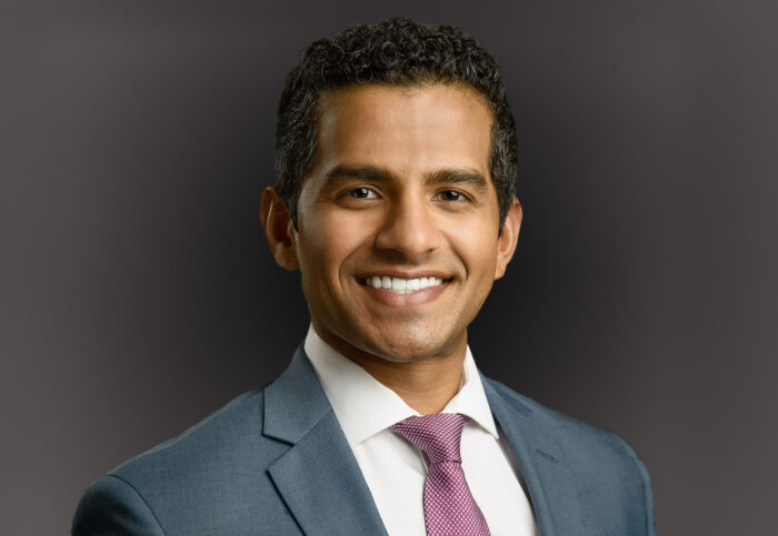 A man in a suit and tie smiles against a plain background, embodying the professionalism of Minnesota hospitals and the dedication of EPPA Health.