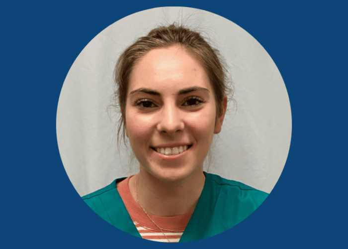 A person smiling warmly, wearing a green scrub top over a white and red-striped shirt, is set against a plain white background within a circular frame. This image reflects the dedication of Minnesota Hospitals' emergency room physicians and EPPA Health professionals.