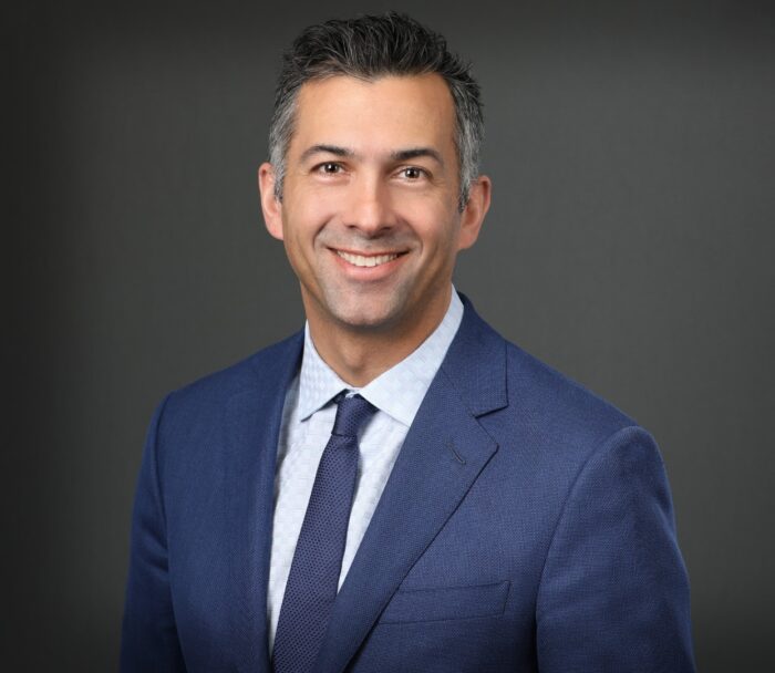 A person in a blue suit and tie, reminiscent of the professionalism exuded by top EPPA Health teams, smiles against a gray background.
