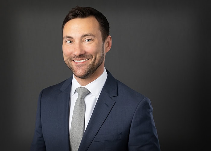 A man in a blue suit and gray tie, perhaps an emergency room physician from EPPA Health, smiles warmly against a gray background.