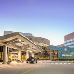 The modern hospital entrance, bearing EPPA Health signage, features a covered driveway and sleek glass facade. A parked vehicle stands nearby, while benches and greenery enhance the inviting atmosphere.