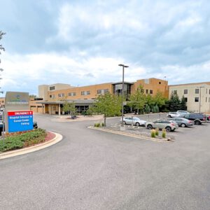 The exterior of the hospital features a parking lot bustling with activity, underscored by signs for emergency services and cancer center parking. A testament to Minnesota Hospitals' commitment, it stands ready to support EPPA Health's dedicated Emergency Room Physicians.
