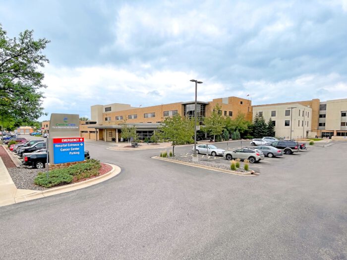 The exterior of the hospital features a parking lot bustling with activity, underscored by signs for emergency services and cancer center parking. A testament to Minnesota Hospitals' commitment, it stands ready to support EPPA Health's dedicated Emergency Room Physicians.