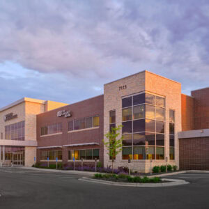 The EPPA Health facility is a modern two-story brick and stone building with large windows, surrounded by a parking lot and lush greenery. Under the cloudy Minnesota sky, its innovative design serves as a welcoming landmark for Emergency Room Physicians and visitors alike.