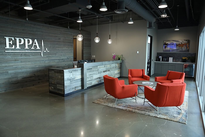 The modern office lobby features a wooden reception desk, red chairs, and a round table on a rug. The wall proudly displays the 