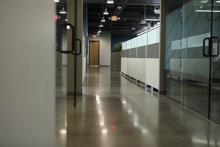 A modern office hallway in EPPA Health, featuring glass doors and cubicles on the right. The polished concrete floors lead to a distant wooden door, reflecting the efficiency and precision akin to Emergency Room Physicians.